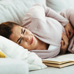 Femme allongée sur un canapé, souffrant de douleurs abdominales, recherchant des solutions naturopathiques pour soulager ses troubles digestifs.