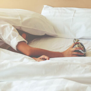 Personne allongée dans un lit, tentant d'éteindre un réveil, illustrant les difficultés à se réveiller dues aux troubles du sommeil.